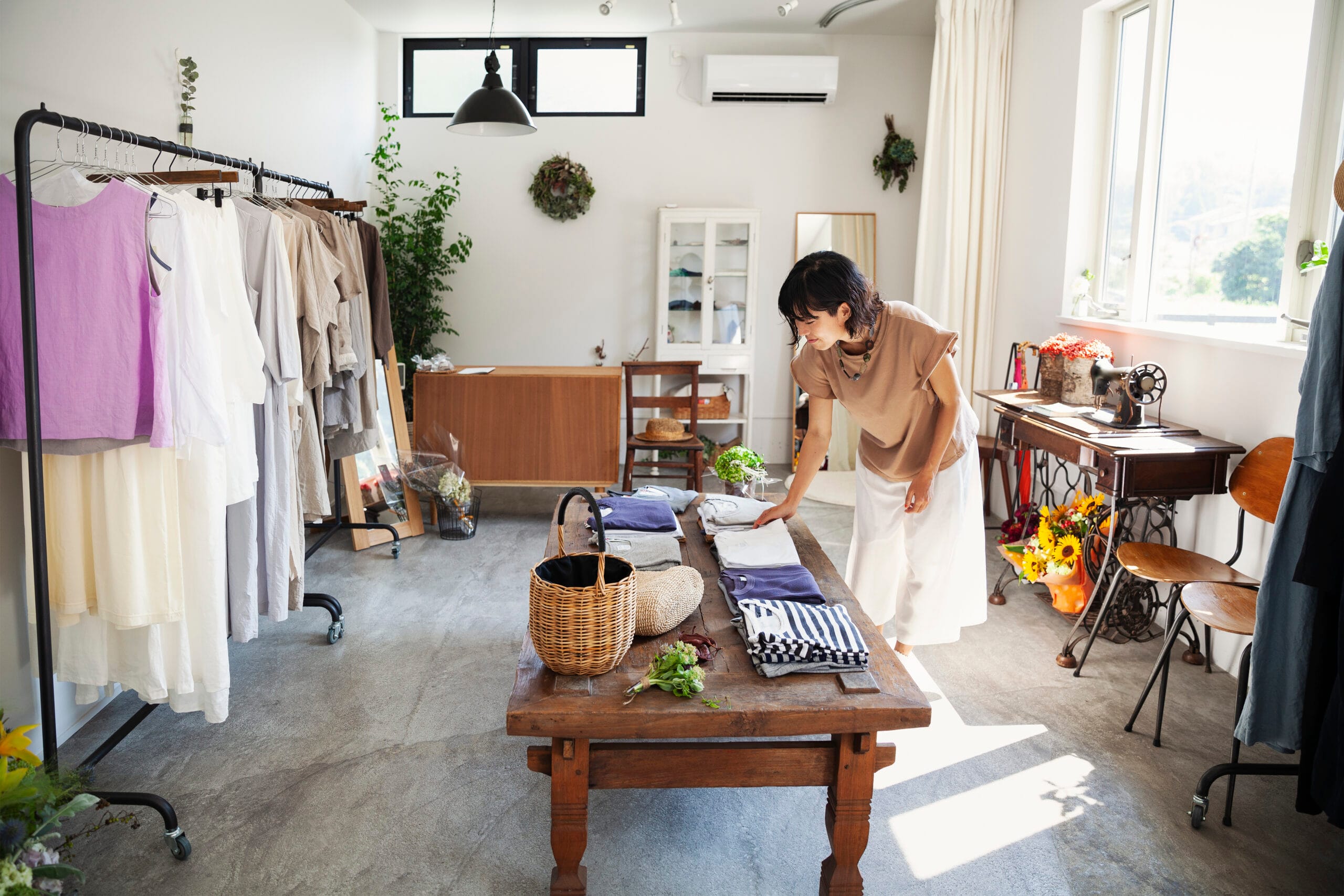Mulher japonesa em pé em uma pequena boutique de moda, olhando camisetas em uma mesa de café.