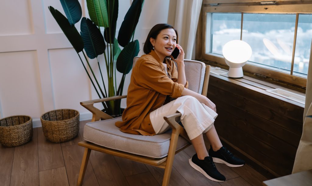 Garota asiática falando no telefone sentada em poltrona com look confortável e casual