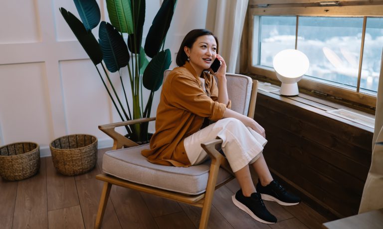 Garota asiática falando no telefone sentada em poltrona com look confortável e casual